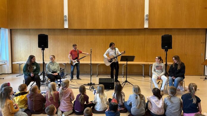 Muusikot esiintyvät Frankfurtin Suomi-koulun lapsille koulun salissa – lapset istuvat lattialla ja seuraavat konserttia.